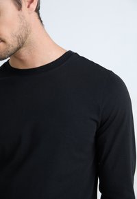 Svart langermet skjorte med rund hals. Laget av myk, glatt stoff, med minimalt med sømmer og en tettsittende design.