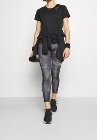 Camiseta atlética negra con un logotipo sutil, leggings de patrón gris oscuro y zapatillas negras. Los leggings tienen costuras laterales y un diseño ajustado.