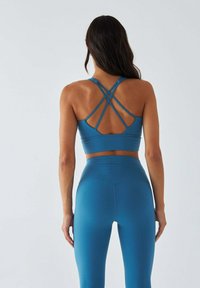 Niebieski sportowy biustonosz z krzyżującymi się ramiączkami oraz dopasowane legginsy z wysokim stanem. Gładka tekstura, bezszwowy design oraz przylegający krój.