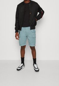 Svart bomberjacka, svart t-shirt, ljusblå cargoshorts och svarta strumpor. Sneakers har en blandning av svart, vitt och grått.