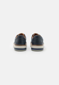 Sneaker blu navy con tallone in pelle liscia, parte superiore in tessuto, suola intermedia beige chiaro in contrasto e fodera arancione, che mette in mostra un design minimalista.