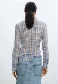 Camisa ligera a cuadros en tonos azul y gris, con diseño de cuello y mangas largas. La parte trasera tiene una sisa y dobladillo curvo.