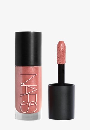 Gloss à lèvres rose nude liquide avec bouchon noir et applicateur, présentant une pointe douce et inclinée en forme de patte de mouche, recouverte de gloss scintillant.