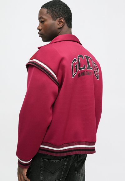 Bordo bomber jakna z črnimi in belimi detajli. Ima ovratnik, rebraste manšete in logo "GCDS" z napisom "MILANO ITALIA" na hrbtni strani.