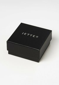 Scatola regalo nera con una superficie testurizzata. Presenta il logo "JETTE" in argento sulla parte superiore. Design minimalista, costruzione robuste.