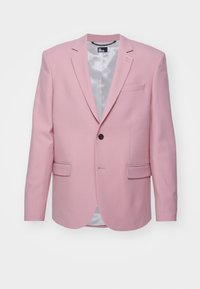 Blazer rose clair en tissu lisse avec un bouton noir unique, deux poches avant et un intérieur doublé en satin. Coupe cintrée.