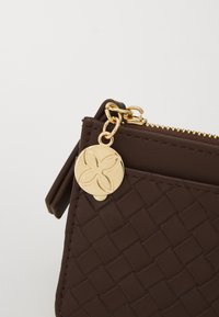 Brown woven leather pouch with a gold zipper and charm. The charm has a floral design, adding detail to the textured surface.