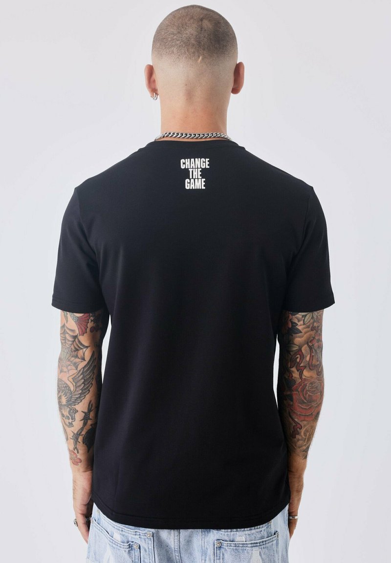 Zwarte katoenen T-shirt met ronde hals en korte mouwen, voorzien van witte tekst "CHANGE THE GAME" op de bovenrug. Eenvoudig ontwerp, geen patronen.