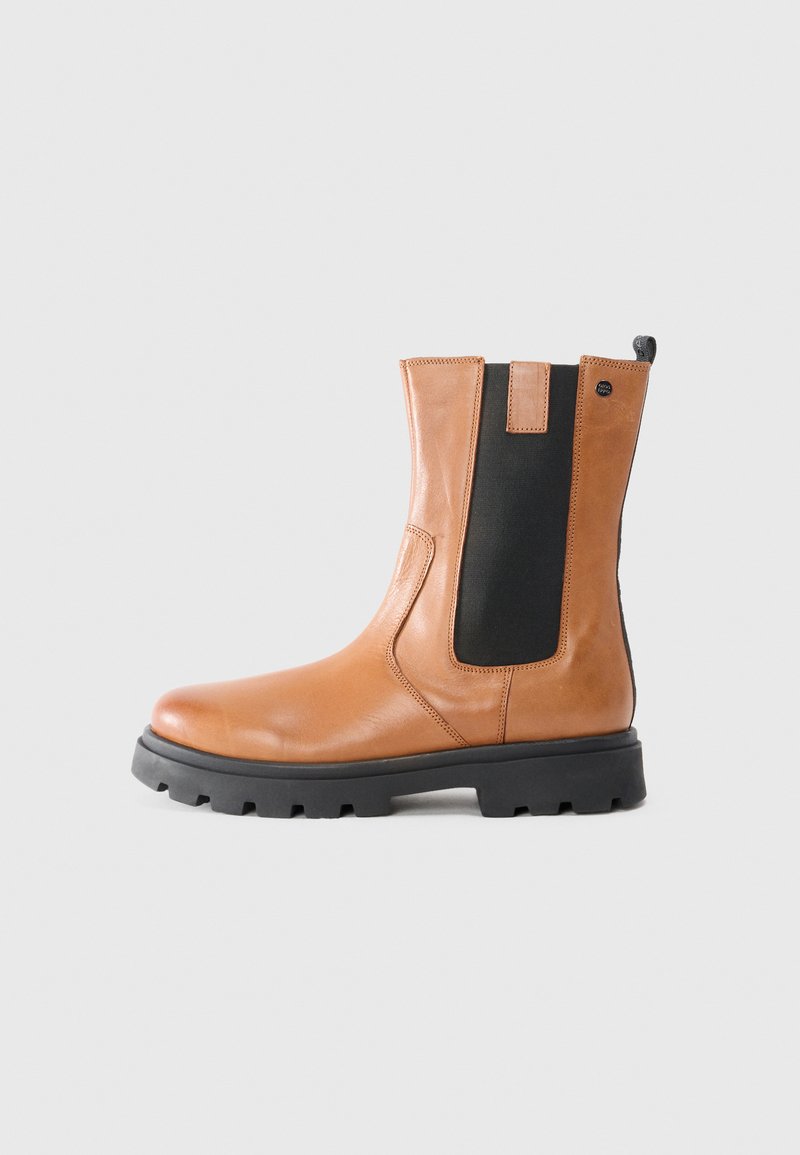 Botín de cuero marrón claro con paneles laterales elásticos negros, punta redondeada y suela gruesa de goma negra con textura antideslizante para mayor agarre.