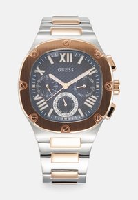 Montre en acier inoxydable argent et or rose avec un cadran sombre texturé, le chiffre romain XII, deux sous-cadrans et un bracelet à maillons plats.