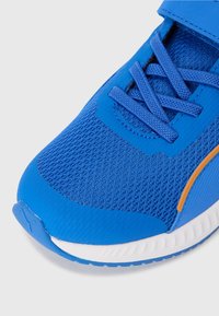 Baskets de sport bleues avec tige en mesh, bout renforcé et accents orange. Présente des lacets texturés et une semelle intermédiaire blanche rembourrée.