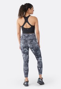 Sujetador deportivo negro con un diseño de espalda en forma de corredor, combinado con leggins ajustados que presentan un patrón marmoleado gris. Llevado con zapatillas de correr negras.