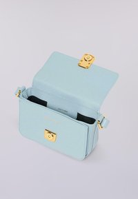 Světle modrá kožená crossbody taška se zlatým klipem, otevřenou klopou a černým interiérem na jednoduchém pozadí.