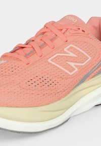 Κοραλλί ροζ αθλητικό παπούτσι New Balance 1080 με πλέγμα και επάνω μέρος από δίχτυ, κλείσιμο με κορδόνια και μαλακή σόλα σε τόνους μπεζ και λευκού.