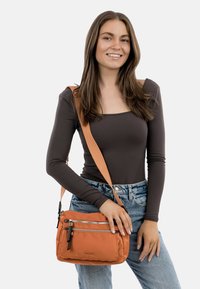 Oranžová crossbody taška s několika zipovými kapsami, vyrobená z odolné látky, s jednoduchým designem a nastavitelným popruhem.
