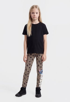 Fille debout face à l’avant, portant un t-shirt noir, des leggings imprimés léopard avec un personnage de dessin animé bleu et des baskets montantes noires.