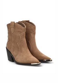Botas de tobillo de gamuza marrón con punteras puntiagudas, costuras de estilo occidental, trabillas para poner y un tacón bajo apilado con acentos metálicos en la puntera.