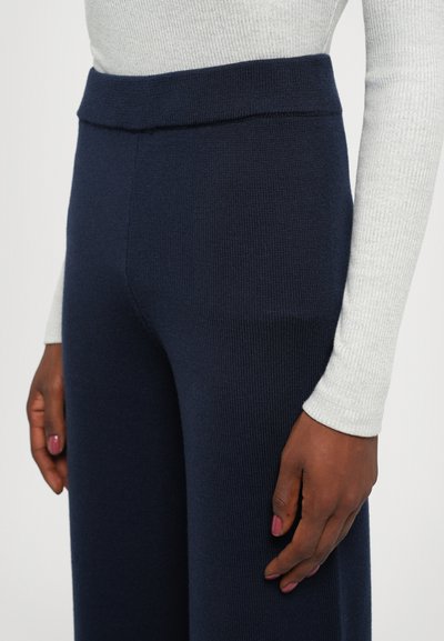 Navy ribbed knit trousers with a wide, flat waistband. The fabric texture is soft, with a slight stretch and a relaxed fit.