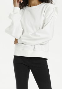 White sweatshirt with puffed sleeves, round neckline, and ribbed cuffs and hem. Material appears soft, with minimal seams and a relaxed fit.