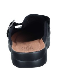 Schwarzer Slipper mit abgerundetem Zehenbereich, ausgestattet mit einem strukturierten Obermaterial, gepolstertem Kragen und einer braunen Innensohle mit eingeprägtem Logo. Dezentes Schnallendetail.