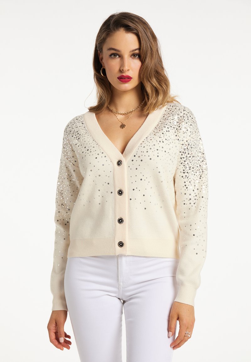 Cardigan crema con un profondo scollo a V, sette bottoni neri sul davanti e pailettes argentate sparse sulle spalle e sulle maniche.