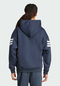 Marineblauwe hoodie met witte drievoudige streepaccenten op de mouwen, inclusief ribgebreide manchetten en zoom. Gemaakt van zachte, gestructureerde stof.