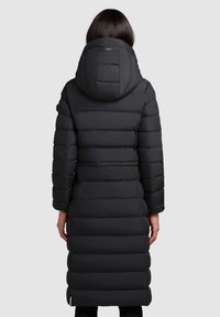 Manteau long noir rembourré avec capuche, présentant une taille cintrée, un matelassage horizontal et une texture lisse. La vue arrière montre un design simple.