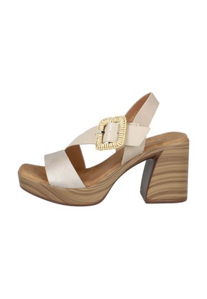 Sandalia beige de punta abierta con tacón bloque de madera, correas anchas que se cruzan sobre el pie y una hebilla grande tejida en la correa del tobillo.