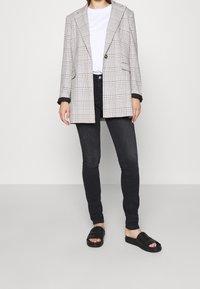 Rutig blazer i grått och vitt med en enda knapp, kombinerad med svarta skinnyjeans och svarta tofflor. Släta texturer genomgående.