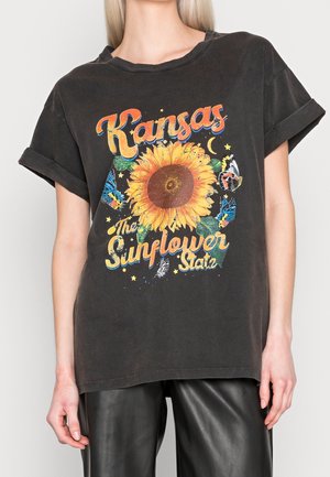 Black oversized t-shirt featuring a sunflower graphic, colorful text "Kansas," and butterflies. Rolled short sleeves and relaxed fit.