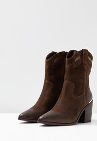Hnědé klučičí kotníkové boty z nubuku s špičatou špičkou, střední blokovou patou a zdobnými panely na svršku. Zip na jedné straně.