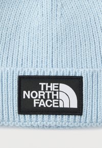 Ανοιχτό μπλε πλεκτό σκουφάκι με ριμπ υφή. Φέρει ένα μαύρο ορθογώνιο αυτοκόλλητο με λευκό κείμενο και λογότυπο της The North Face.