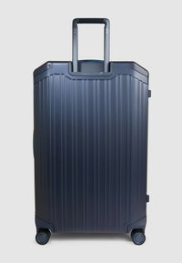 Valigia rigida blu navy con texture a nervature verticali, manico estensibile, quattro ruote e maniglia laterale per un facile trasporto.