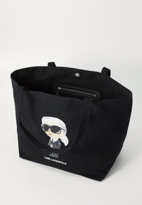 Black canvas tote bag featuring a cartoon graphic of a figure in sunglasses. Open top with two carrying straps and inner zip pocket.