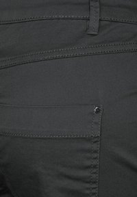 Pantalones ajustados negros hechos de una tela suave, que cuentan con un bolsillo trasero con un sutil detalle de costura y un acento de botón metálico.