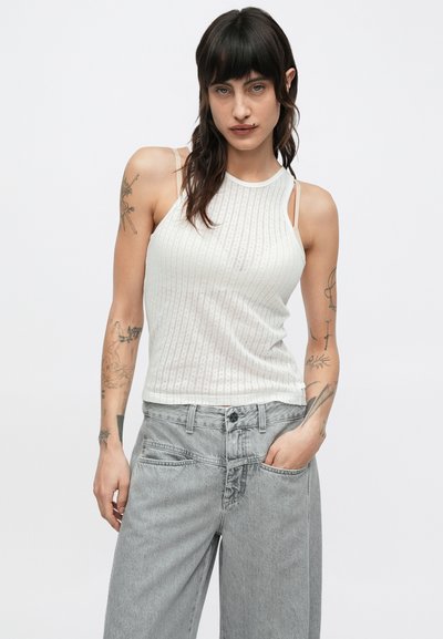 Débardeur blanc côtelé avec fines bretelles et encolure ronde, associé à un jean gris clair à jambes larges, doté de poches avant et d'une fermeture par bouton.