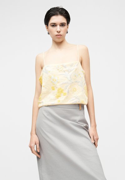Κίτρινο κεντητό τοπ με λουλουδάτα σχέδια, λεπτές ράντες, σε συνδυασμό με μια γκρι φούστα με ομαλή υφή και πλαϊνή λεπτομέρεια.