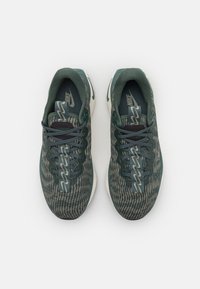 Scarpe sportive verdi con una tomaia in maglia testurizzata, dettagli grigi e una suola bianca. Presentano lacci e un logo visibile sulla linguetta.