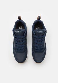 Navy blue athletic shoes with a textured surface, featuring a lace-up design, white sole, and brown accents on the heel tab.
