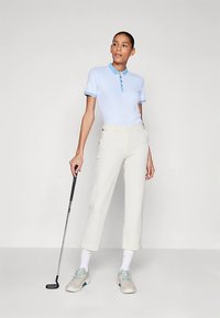 Jasnoniebieska koszulka polo z teksturowanym wzorem, zapinanym na guziki kołnierzykiem oraz kontrastującym obszyciem; w zestawie z kremowymi, krótkimi spodniami do golfa i szarymi butami.