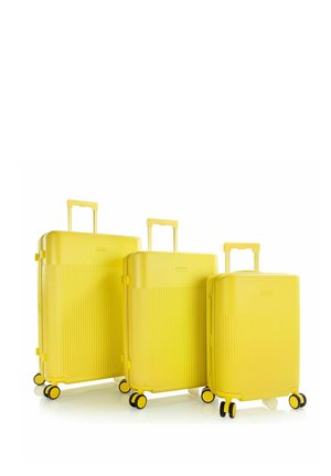 Tre valigie rigide gialle con manici telescopici e quattro ruote, disposte dalla più grande alla più piccola su sfondo bianco.