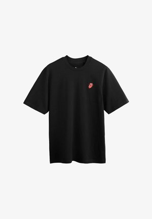 Schwarzes T-Shirt mit kurzen Ärmeln und einem kleinen roten Rolling-Stones-Zungen- und Lippenlogo auf der oberen linken Brust.