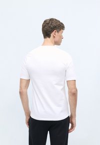 White cotton t-shirt with a rounded neckline, short sleeves, and a smooth texture. Displayed from the back against a light background.