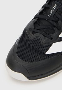 Chaussure de sport noire avec tige en mesh et synthétique, dotée d'accents blancs, d'un motif texturé et d'un système de lacets noirs. Semelle en caoutchouc durable.