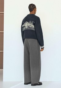 Donkerblauwe sweatshirt met een stadsgezicht op de achterkant, gecombineerd met losse grijze broek. Voorzien van geribde manchetten en een comfortabele pasvorm.