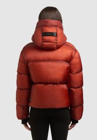 Czerwona pikowana kurtka puchowa z wysokim kołnierzem i kapturem, z przeszywanym wypełnieniem, ściągaczami na rękawach oraz czarną naszywką z logo na plecach.