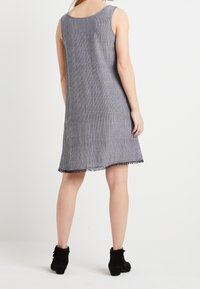 Ärmelloses gestreiftes Kleid in Blau und Weiß mit einem gewellten Saum. Kombiniert mit schwarzen Knöchelstiefeln. Leichter Stoff, lockerer Sitz.