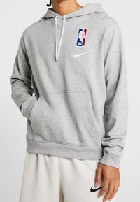 Sweat à capuche Nike gris en tissu doux, doté d'une poche frontale, d'une capuche ajustable et du logo NBA sur la poitrine en bleu, rouge et blanc.
