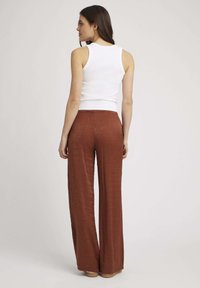 Débardeur blanc sans manches et pantalon large couleur rouille en tissu texturé, avec une taille haute et une coupe fluide.