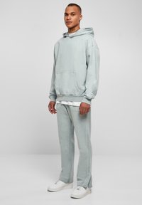 Felpa blu chiaro con tasca a marsupio e polsini elasticizzati, abbinata a pantaloni della tuta coordinati. Tessuto morbido, vestibilità rilassata e sneakers bianche.